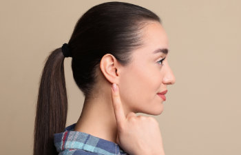 young woman pointing at her ear on beige background